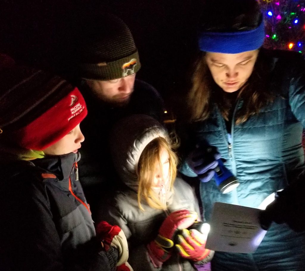Family of four singing a Christmas carol with a flashlight.