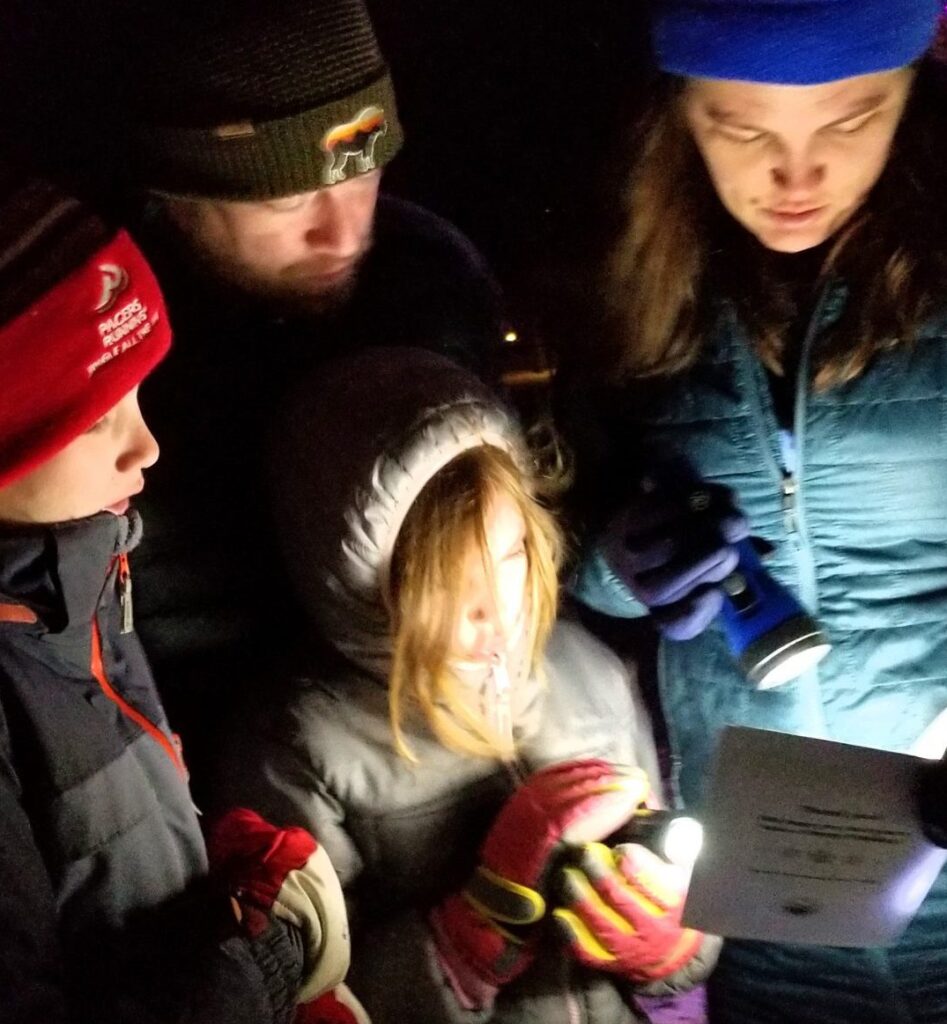 Family of four singing a Christmas carol with a flashlight.
