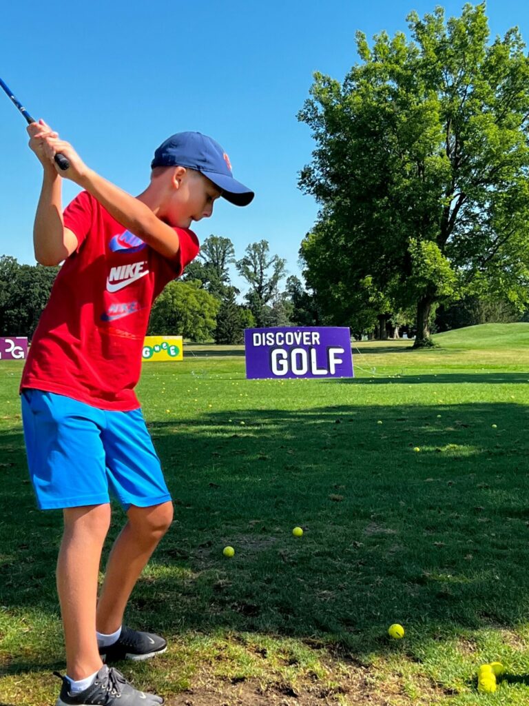 middle school aged boy hitting golf balls towards colorful targets during a golf lesson