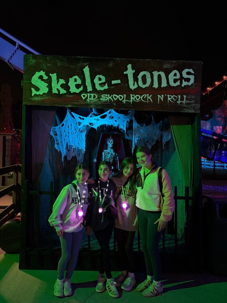 Four teen girls standing in front of haunted house smiling at camera