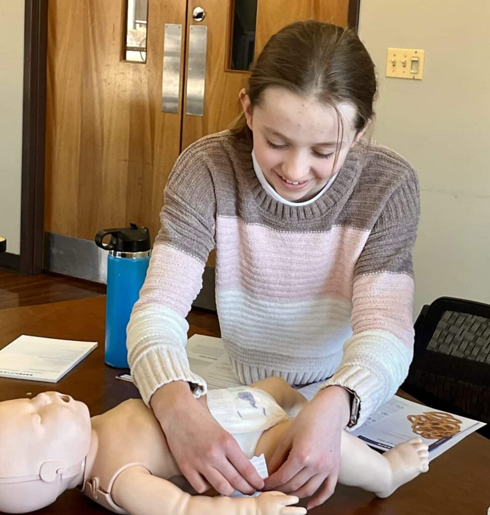 Middle school aged girl practicing putting a diaper on a baby.