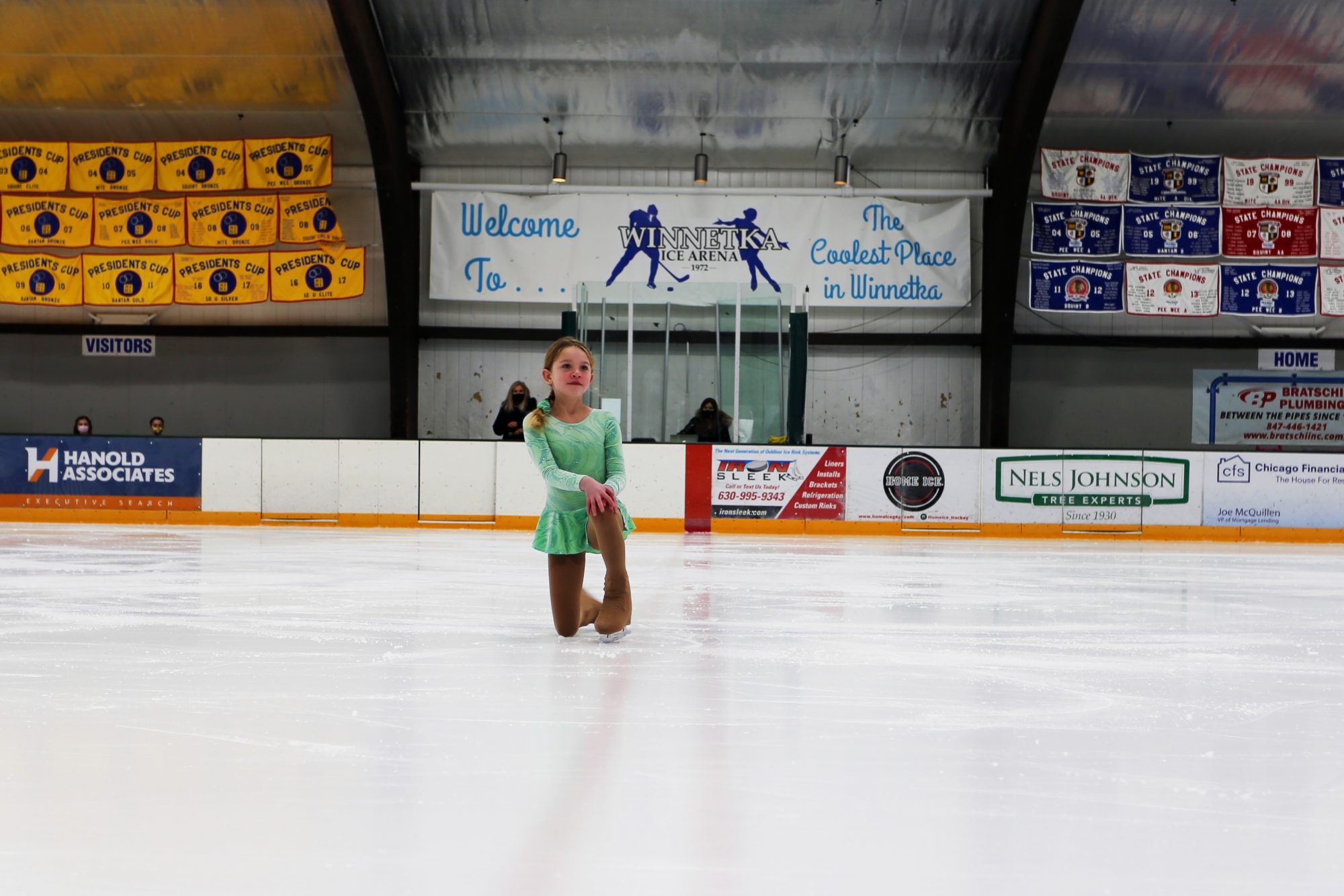 young girl in a green dress performing an ice skating routine
