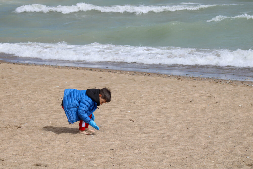 Little boy with brown hair, wearing a winter coat, playing looking in the sand at the beach.