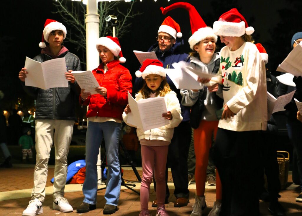 Group of people with Santa hats singing Christmas carols.