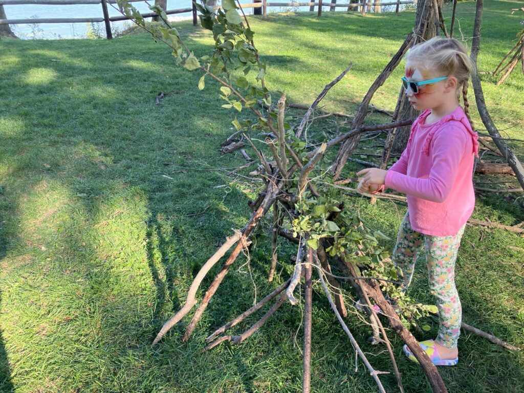 Young girl putting together a small fort made of sticks and flowers.
