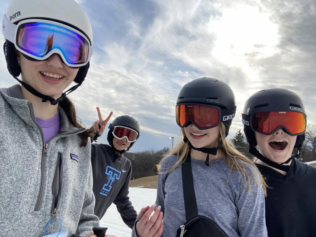 Four young kids smiling together wearing ski goggles and helmets.