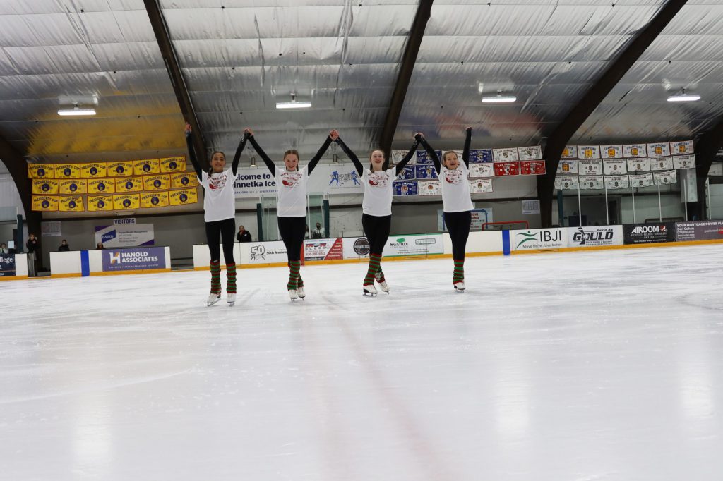 four teen girls holding their hands up in the air to take a bow after performing an ice skating routine