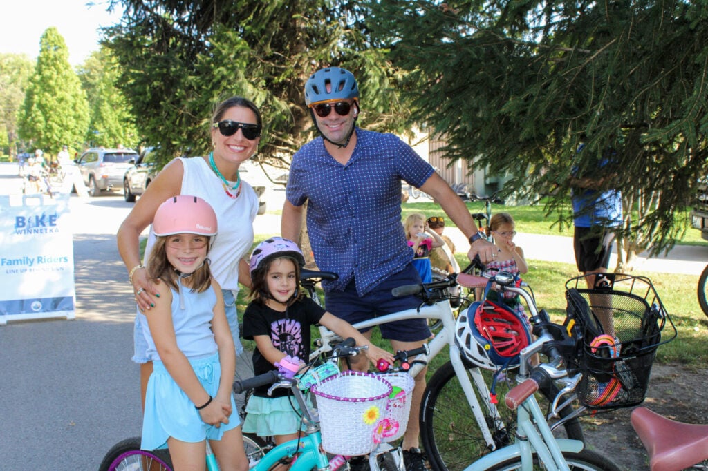 Family of two adults and two young girls standing with their bikes and smiling at camera