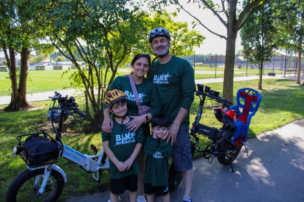 Family of two adults and two young boys standing together in front of their bikes smiling at camera