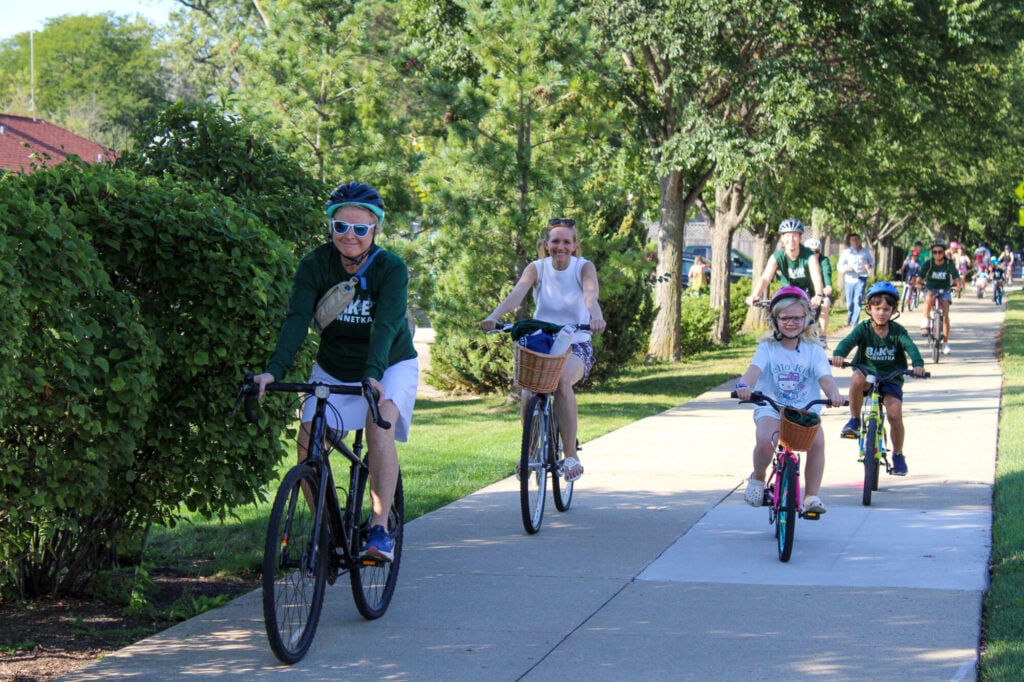 Two adults and two children biking towards the camera on sidewalk smiling