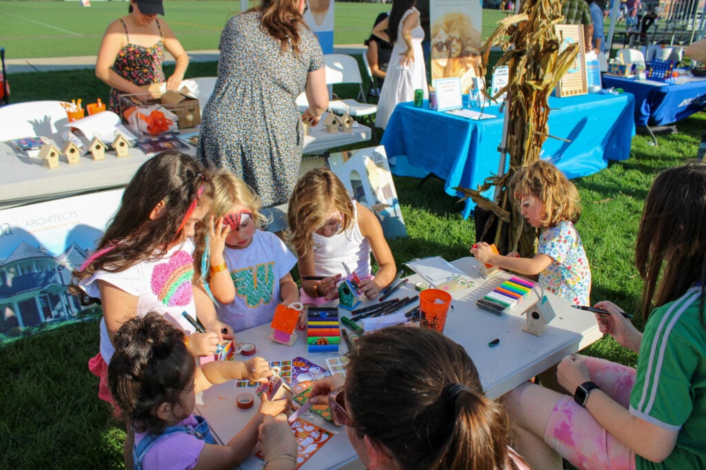 Group of young girls with their faces painted doing various crafts around a table