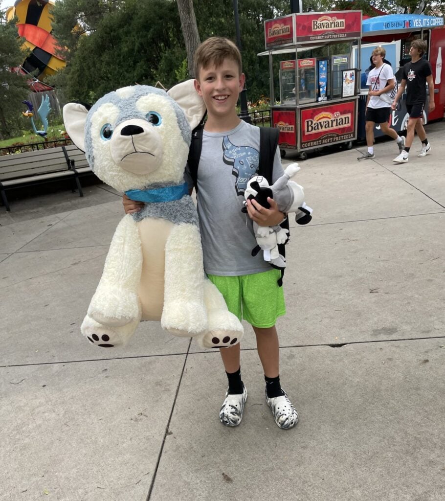 middle school boy holding up his prizes of an oversized stuffed animal and a small stuffed animal he won at Six Flags