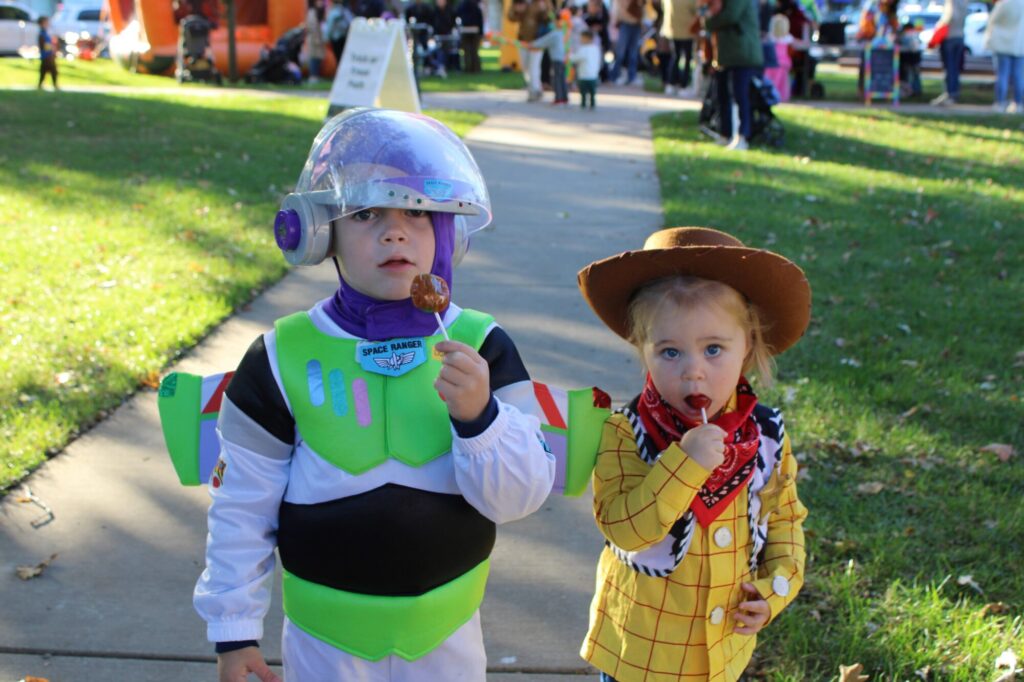 Little boy dressed as Buzz Lightyear and girl dressed as Woody from toy story licking Lolly pops