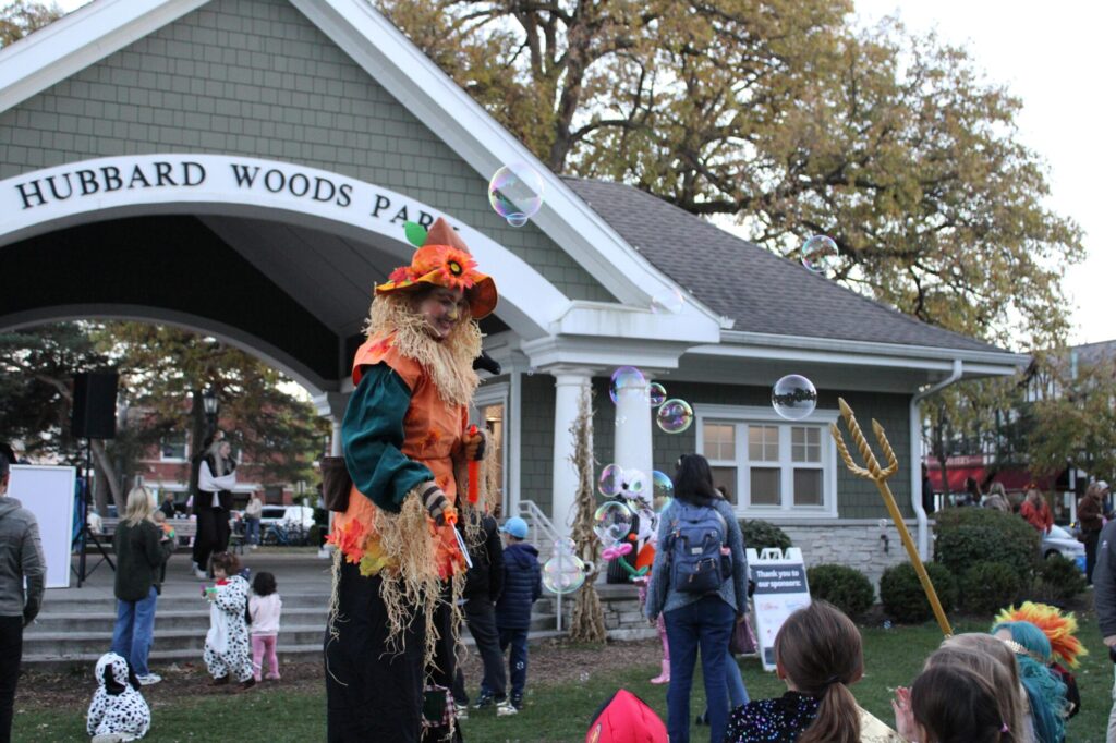 Woman dressed as a pumpkin on stilts smiling at children and blowing bubbles