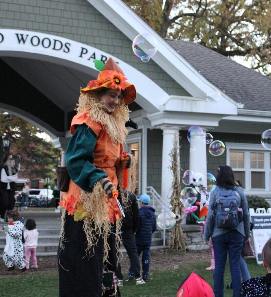 Woman dressed as a pumpkin on stilts smiling at children and blowing bubbles