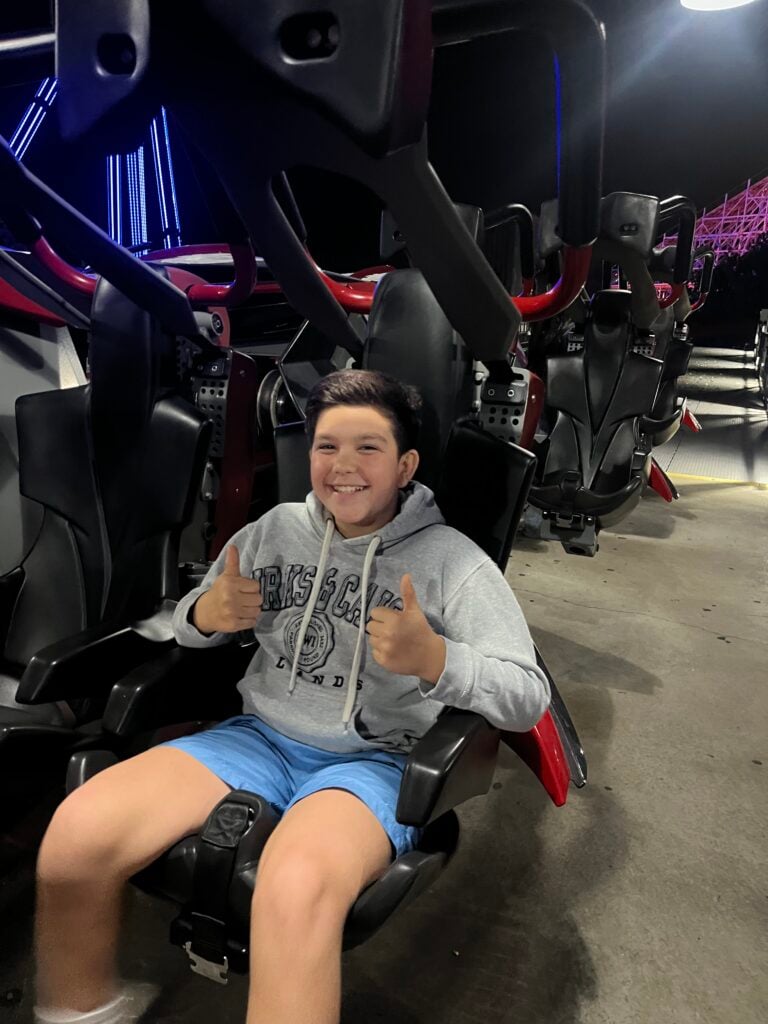 Young boy sitting on roller coaster ride smiling and giving a thumbs up