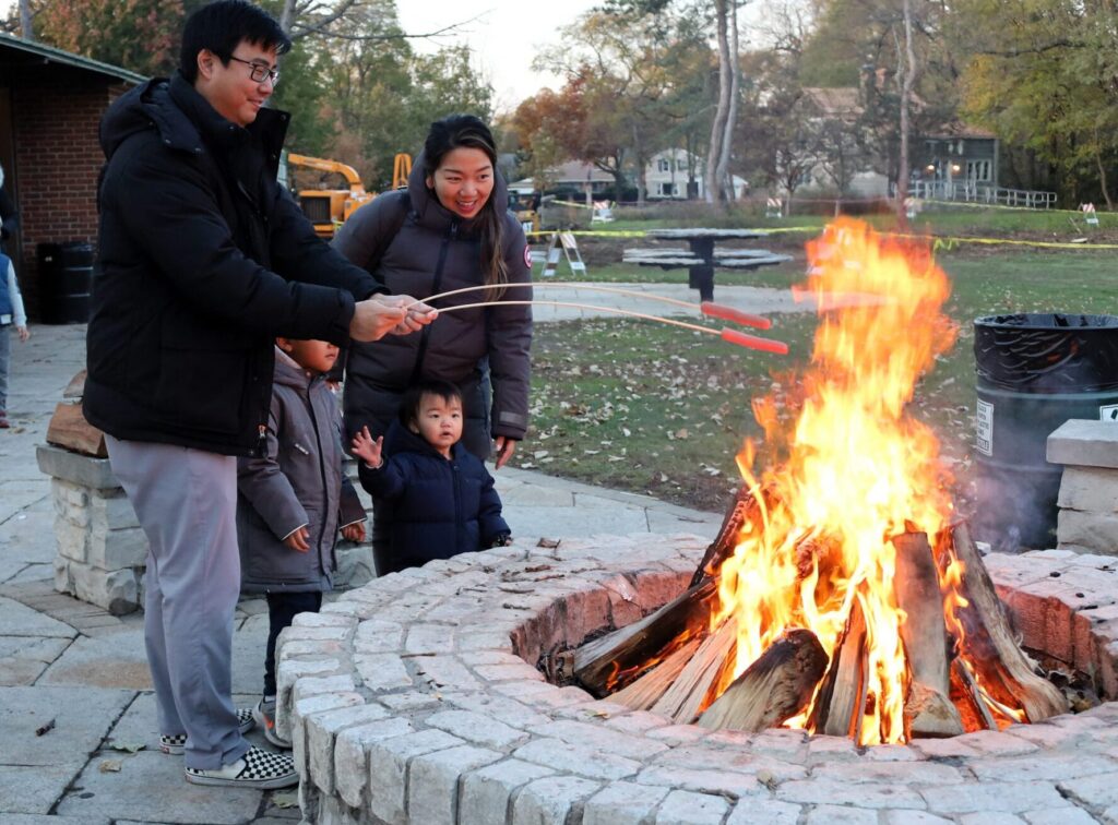 A family of four roasting hotdogs over a firepit outdoors.