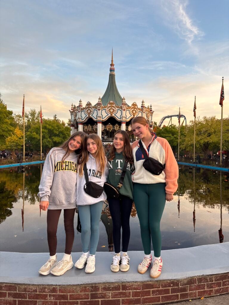 Four teen girls standing in front of Six Flags pool and carousel smiling