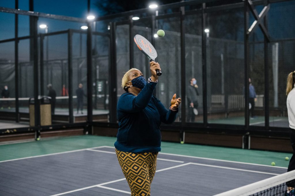 Adult women serving a ball on an outside platform court.