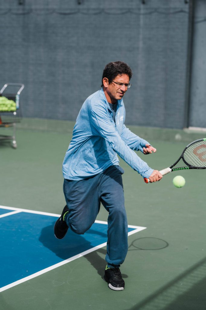 Adult male play tennis outside.