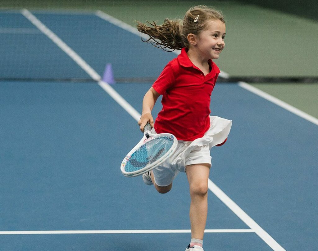 Little girl running along a tennis court.