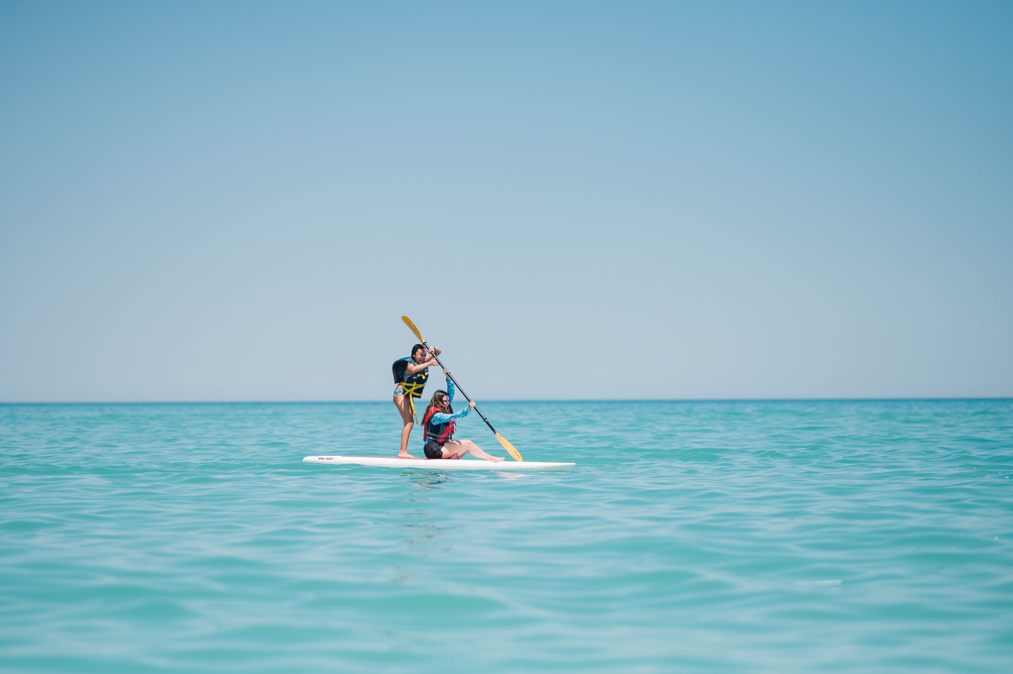 two middle school aged girls on a paddle board on Lake Michigan